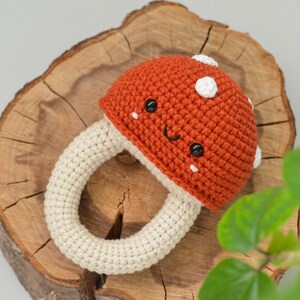 May include: A crocheted mushroom toy with a white ring and a red cap. The mushroom has a smiling face with black eyes and white cheeks.