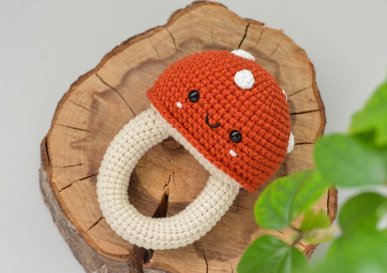 May include: A crocheted mushroom toy with a white ring and a red cap. The mushroom has a smiling face with black eyes and white cheeks.