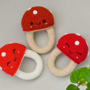 May include: Three crocheted mushroom-shaped teethers with white rings. The mushrooms are red with white polka dots and have embroidered smiling faces.