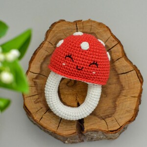 May include: A crocheted mushroom-shaped baby teether with a white ring and a red cap with white polka dots and a smiling face.
