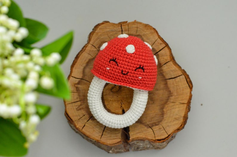 May include: A crocheted mushroom-shaped baby teether with a white ring and a red cap with white polka dots and a smiling face.