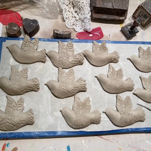 Może przedstawiać: Dziesięć ceramicznych ozd&oacute;b w kształcie gołębia z misternymi wzorami kwiatowymi. Gołębie są ułożone w dw&oacute;ch rzędach na szarej powierzchni z niebieską obw&oacute;dką.