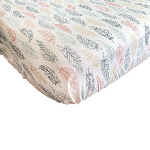May include: A white fitted crib sheet with a colorful feather pattern. The sheet is made of soft, breathable fabric and is perfect for a nursery.