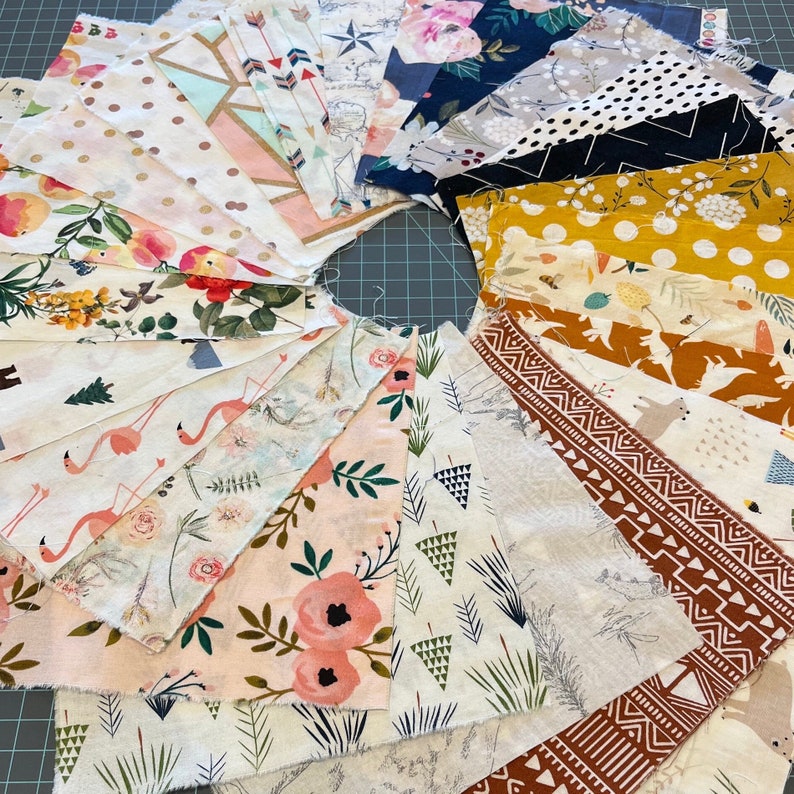 May include: A collection of fabric swatches arranged in a circular pattern. The swatches feature various floral, geometric, and animal prints in colors like pink, white, gold, and navy. The fabrics are likely cotton or a similar material, suitable for quilting or crafting projects.