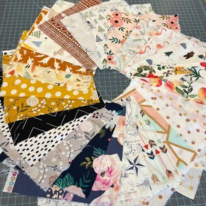 May include: A circular arrangement of fabric squares with various patterns. Designs include floral, geometric, and animal prints in colors like yellow, pink, and navy. The fabrics are arranged on a gray cutting mat.