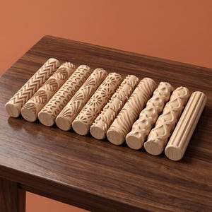 May include: A collection of ten cylindrical wooden rolling pins arranged in a row. Each rolling pin features a distinct carved pattern, including chevron, leaf, floral, wave, and vertical line designs, showcasing natural light wood grain textures.