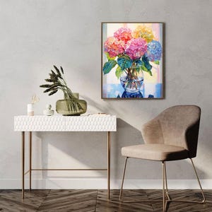 May include: A framed watercolor painting of a bouquet of hydrangeas in a clear glass vase. The flowers are in shades of pink, orange, yellow, and blue, with green leaves. The painting is displayed on a gray wall.