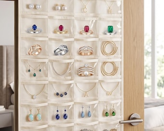 May include: A cream-colored hanging jewelry organizer with multiple clear plastic pockets, suspended by a metal hook over a door. The organizer features a BEB brand label and contains various rings, necklaces, bracelets, and earrings stored inside.