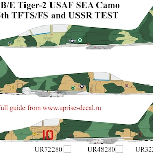 Könnte beinhalten: Illustration von drei F-5B/E Tiger-2 USAF SEA Camo Kampfflugzeugen. Die Flugzeuge sind in Tarnmustern aus Grün, Beige und Braun lackiert. Der Text "F-5B/E Tiger-2 USAF SEA Camo 425th TFTS/FS and USSR TEST" ist enthalten.