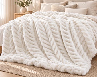May include: A plush, off-white faux fur throw blanket featuring a prominent, raised herringbone or braided cable knit pattern. The thick, soft-textured fabric is draped over a bed, showcasing its deep, dimensional ridges and soft, fuzzy surface.