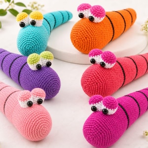 Puede incluir: Seis juguetes de gusanitos tejidos a mano en colores brillantes como turquesa, naranja, morado, rojo, rosa claro y rosa oscuro. Cada gusano tiene dos ojos grandes y redondos con pupilas negras y anillos negros cosidos en sus cuerpos.