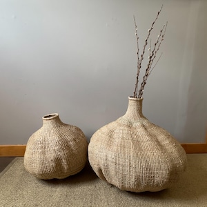 May include: Two woven baskets in the shape of a bulb, one larger than the other, with a bouquet of dried branches in the larger basket.