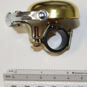 May include: A gold bicycle bell with a black rubber clamp. The bell is approximately 2 inches in diameter.