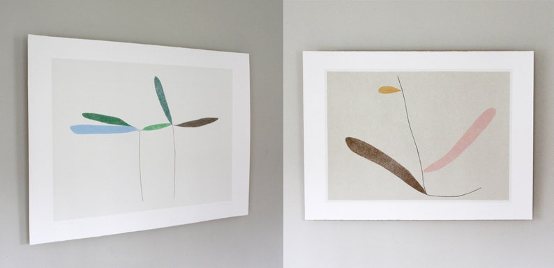 May include: Two framed abstract art prints with minimalist line drawings of stylized plants in shades of green, blue, brown, pink, and yellow on a white background.