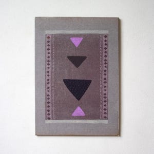 May include: A rectangular wall art piece featuring a muted gray background with a central vertical panel in a darker shade. The panel displays four stacked triangles in alternating purple and black, flanked by two vertical borders of diamond patterns.