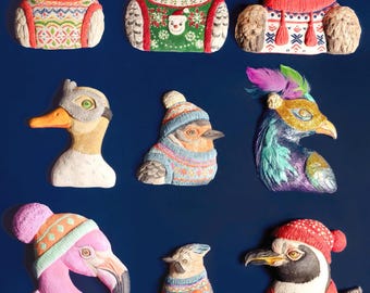 May include: A collection of nine whimsical bird figurines, each uniquely designed. The birds are adorned with sweaters, hats, and scarves in various colors and patterns. The figurines are set against a deep blue background, creating a festive and decorative theme.