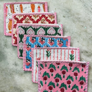 May include: A stack of six rectangular, quilted pouches with zipper closures. Each pouch features a unique patterned fabric in various colors, including white with orange fish, red with floral designs, and pink with green berries. The edges are trimmed with pink and white striped fabric.