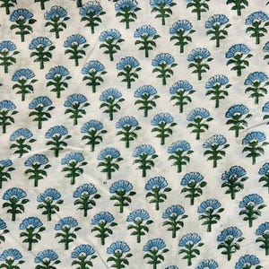 May include: White fabric with a repeating pattern of blue floral designs. Each flower has a detailed petal arrangement and is set against a backdrop of green stems and leaves. The fabric is likely cotton or linen.