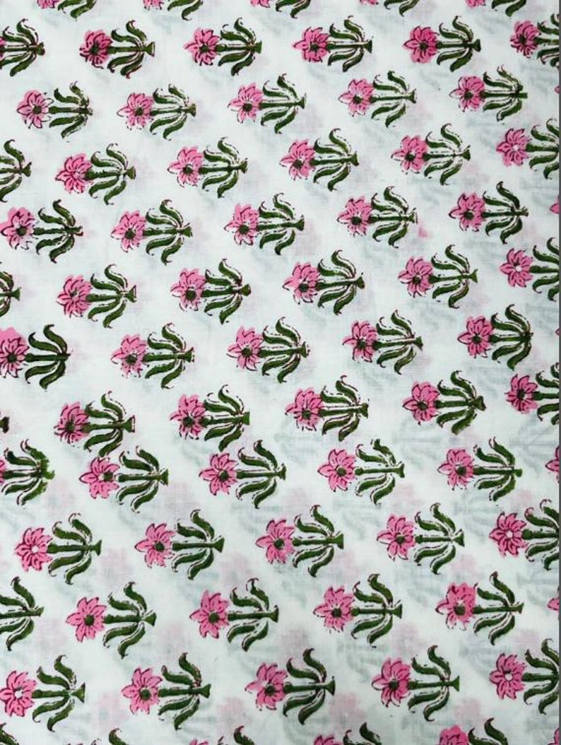 May include: White fabric with a repeating pattern of pink flowers and green leaves. The floral design is evenly spaced across the fabric, creating a consistent and visually appealing texture. The flowers have multiple petals.