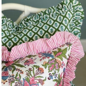 May include: Close-up of decorative throw cushions with floral and geometric patterns. One cushion features a white background with pink and blue floral designs, while another has a green geometric pattern. All cushions have ruffled edges.