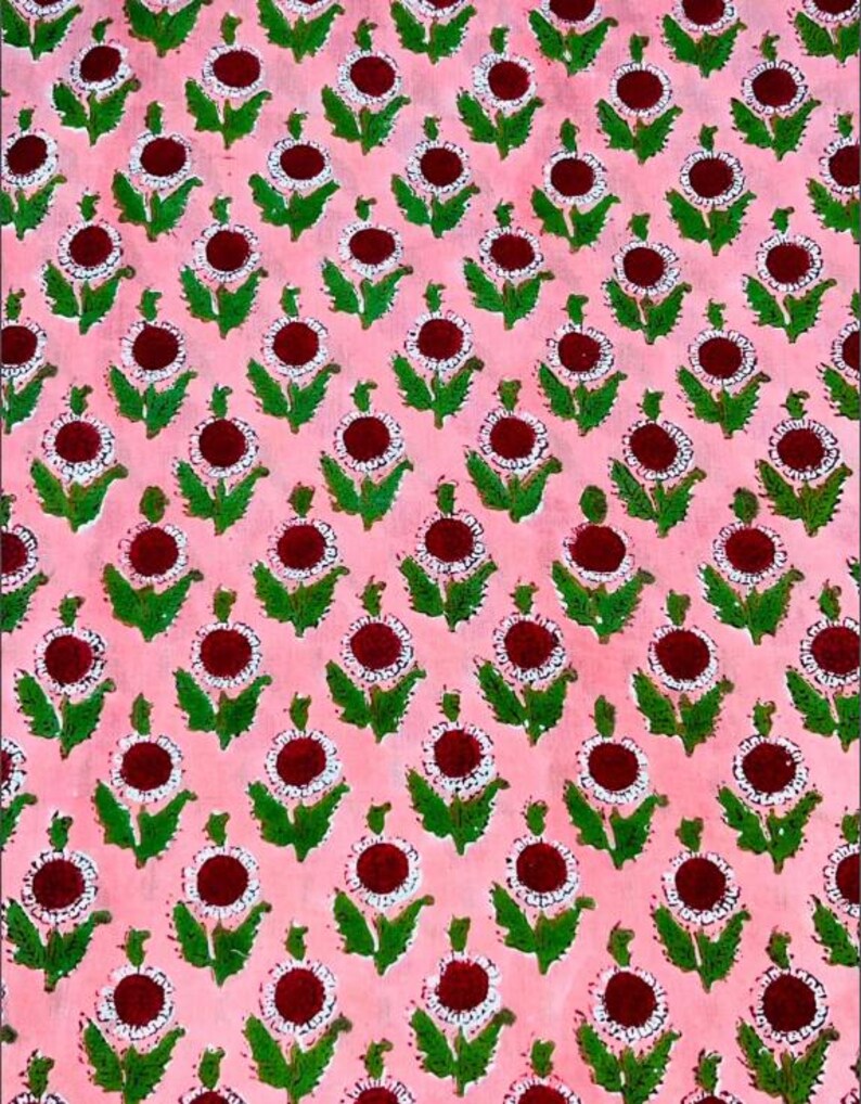 May include: A repeating floral pattern on a pink background. The design features dark red circular centers surrounded by white dots, green leaves, and stems. This textile design is suitable for fabric, wallpaper, or other decorative applications.
