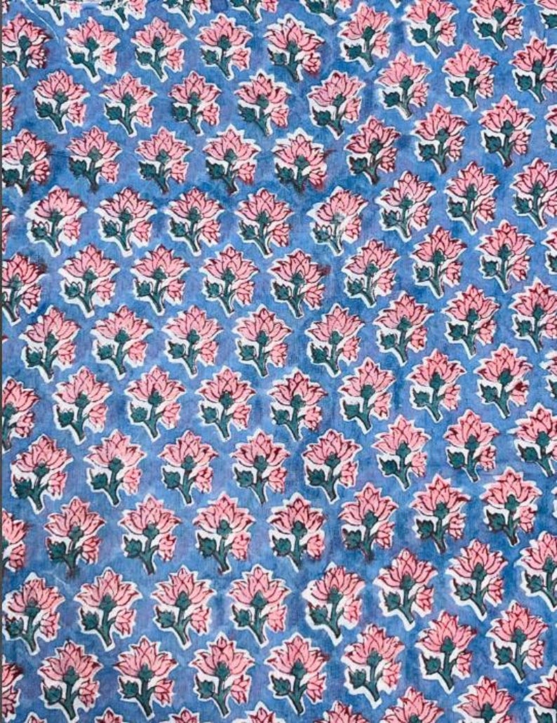 May include: A blue fabric with a repeating pattern of pink floral designs. Each flower has a detailed outline and green leaves. The overall effect is a delicate, yet bold, textile pattern.