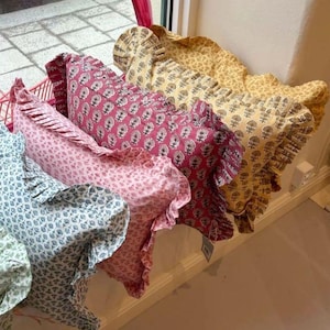 Puede incluir: Una colección de cojines rectangulares con bordes de volantes y estampados florales de bloque. Los cojines se muestran en fila, exhibiendo una variedad de colores que incluyen azul claro, rosa suave, magenta intenso y amarillo cálido.