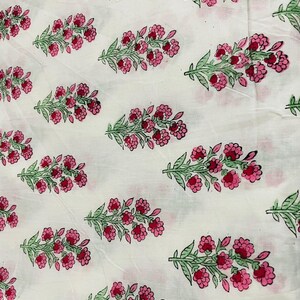 May include: White fabric with a repeating pattern of pink flowers and green leaves. The floral design is evenly spaced across the fabric, creating a visually appealing and symmetrical arrangement. The flowers are a vibrant pink, and the leaves are a soft green.