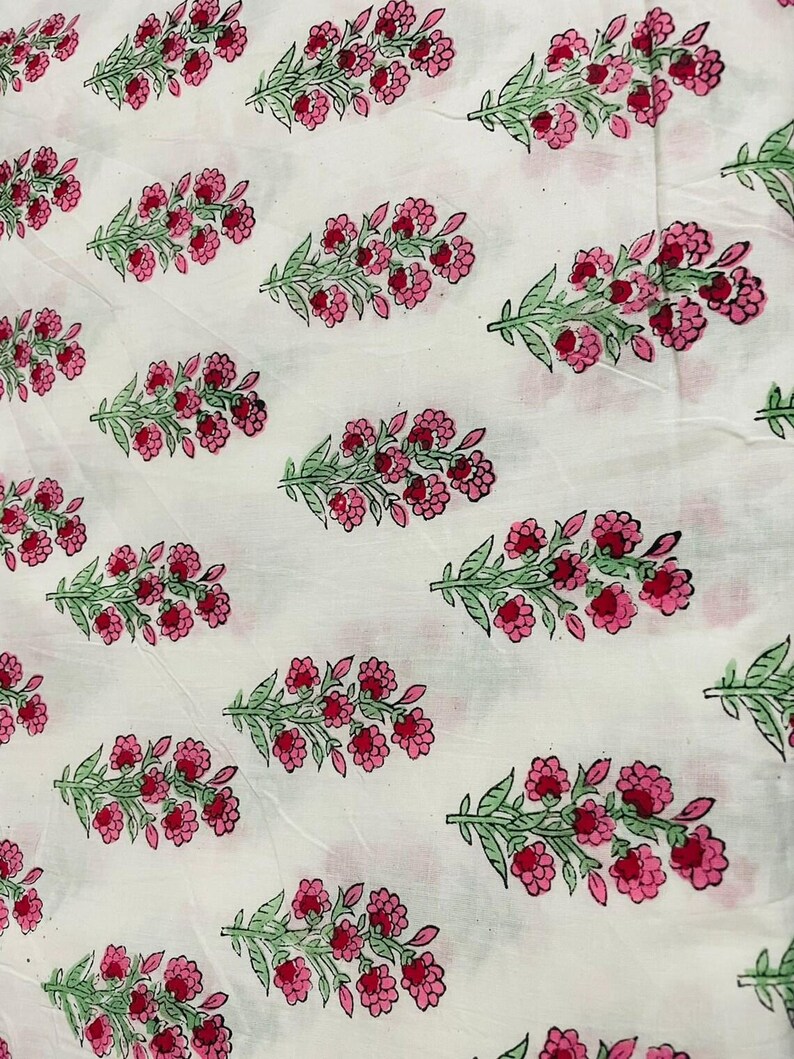 May include: White fabric with a repeating pattern of pink flowers and green leaves. The floral design is evenly spaced across the fabric, creating a visually appealing and symmetrical arrangement. The flowers are a vibrant pink, and the leaves are a soft green.