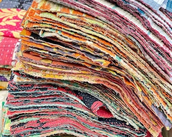 May include: A stack of colorful fabric scraps in various patterns and colors, including orange, red, green, and blue. The edges of the fabric are frayed, suggesting a vintage or handmade quality. The textiles appear to be repurposed or upcycled.