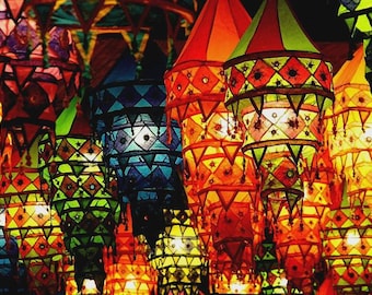 May include: A collection of colorful, hanging lanterns in shades of red, orange, yellow, green, and blue. Each lantern has a geometric pattern and a conical top. The lanterns are lit from within, creating a warm glow.