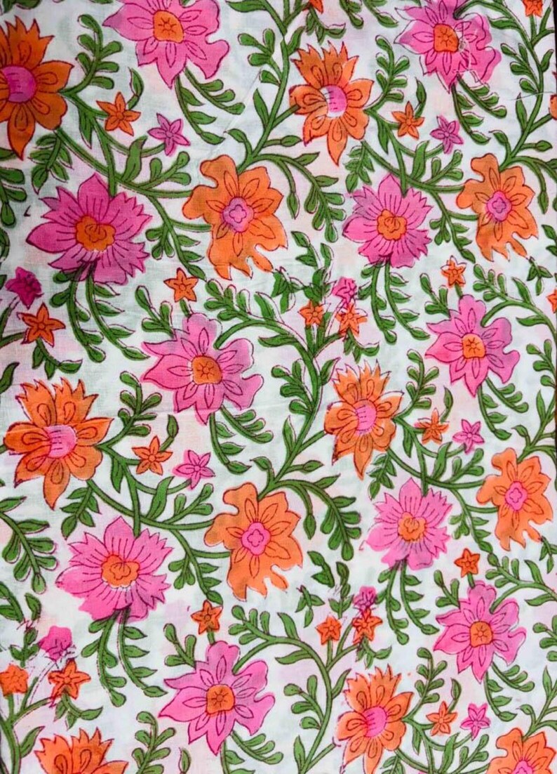 May include: White fabric with a repeating floral pattern. The design features pink and orange flowers with green stems and leaves. Small pink flowers are scattered throughout the design.