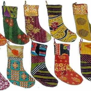 Puede incluir: Diez calcetines navideños dispuestos en dos filas, cada uno confeccionado con tela acolchada y costuras kantha. Los calcetines presentan una variedad de patrones coloridos, incluyendo estampados florales, geométricos y abstractos en tonos rojos, verdes, amarillos y azules, con puños en contraste.