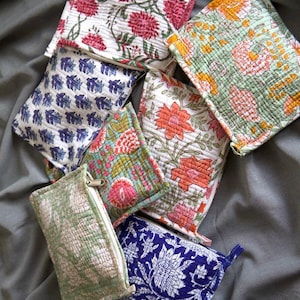 Könnte beinhalten: Eine Sammlung farbenfroher, gesteppter Beutel mit floralen Mustern. Die Beutel zeigen verschiedene Designs, darunter rote, rosa, orange und blaue Blumen auf weißen, grünen und blauen Hintergründen. Jeder Beutel hat einen Reißverschluss.