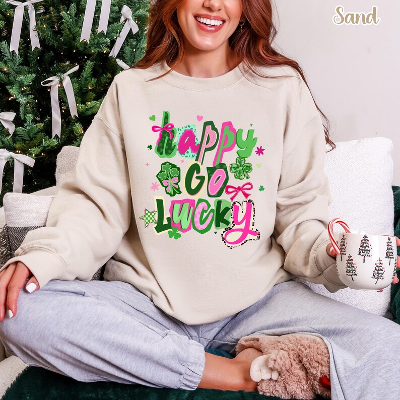 A woman wearing a white sweatshirt with a colorful graphic design and text, sitting on a couch and holding a mug.