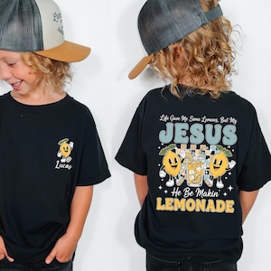 A young boy wearing a black t-shirt with a graphic design and text on the back, smiling and looking at the camera.