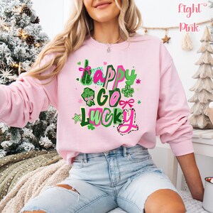 A woman wearing a pink sweatshirt with a colorful graphic design that says "Happy Go Lucky" on it.