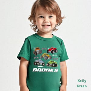 A young child wearing a green t-shirt with a graphic of monster trucks printed on it, smiling at the camera.