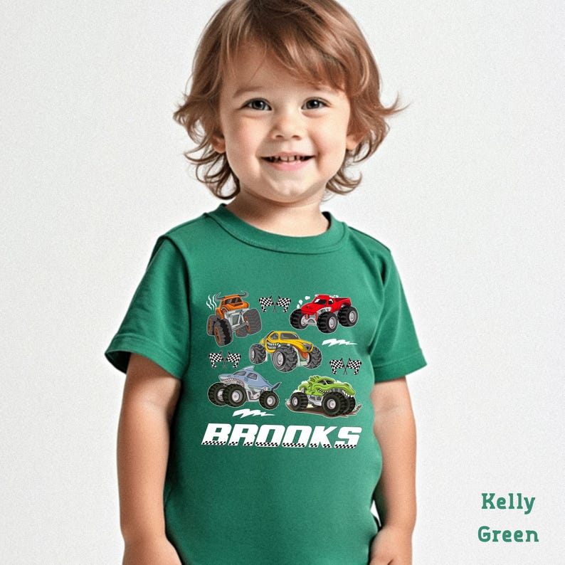 A young child wearing a green t-shirt with a graphic of monster trucks printed on it, smiling at the camera.
