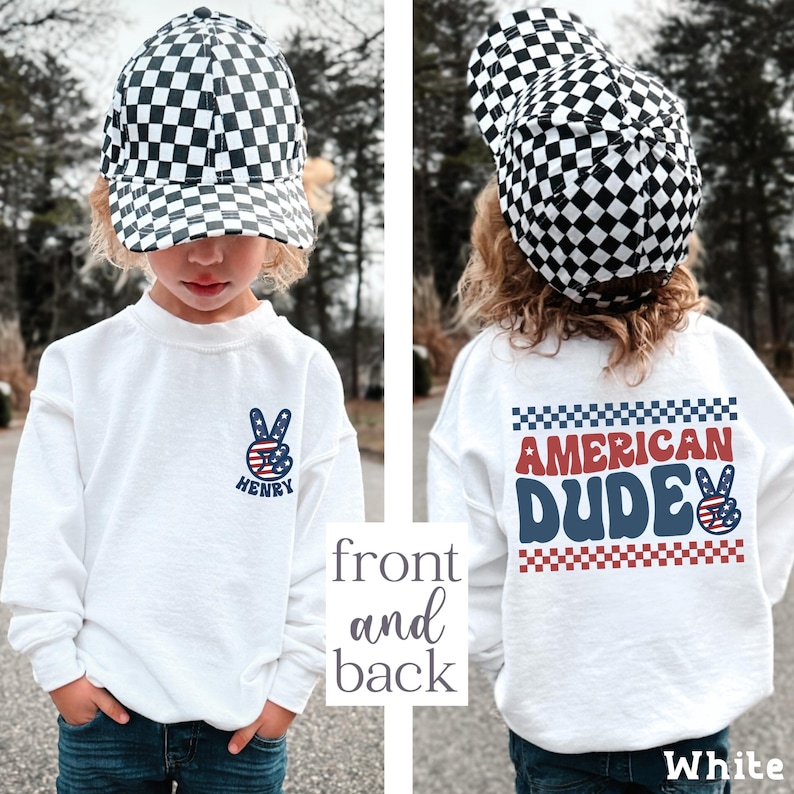 A young child wearing a white sweatshirt with a checkered hat and a peace sign on the front, and a white sweatshirt with the text "American Dude" on the back.