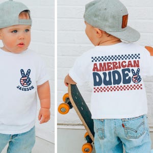 A young child wearing a white t-shirt with a peace sign and the name "Jackson" printed on it, holding a skateboard.