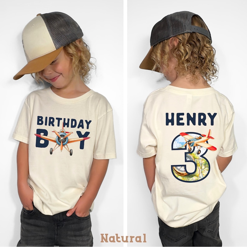 A young boy wearing a white t-shirt with a graphic of an airplane and the text "Birthday Boy" and the number "3" on the back.