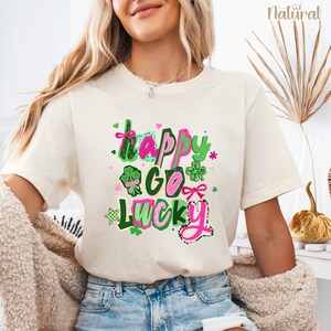 A woman wearing a white t-shirt with a colorful graphic design that says "Happy Go Lucky" and includes various symbols and text.