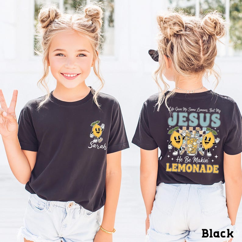 A young girl with blonde hair is smiling and posing for the camera, wearing a black t-shirt with a lemon graphic and text.