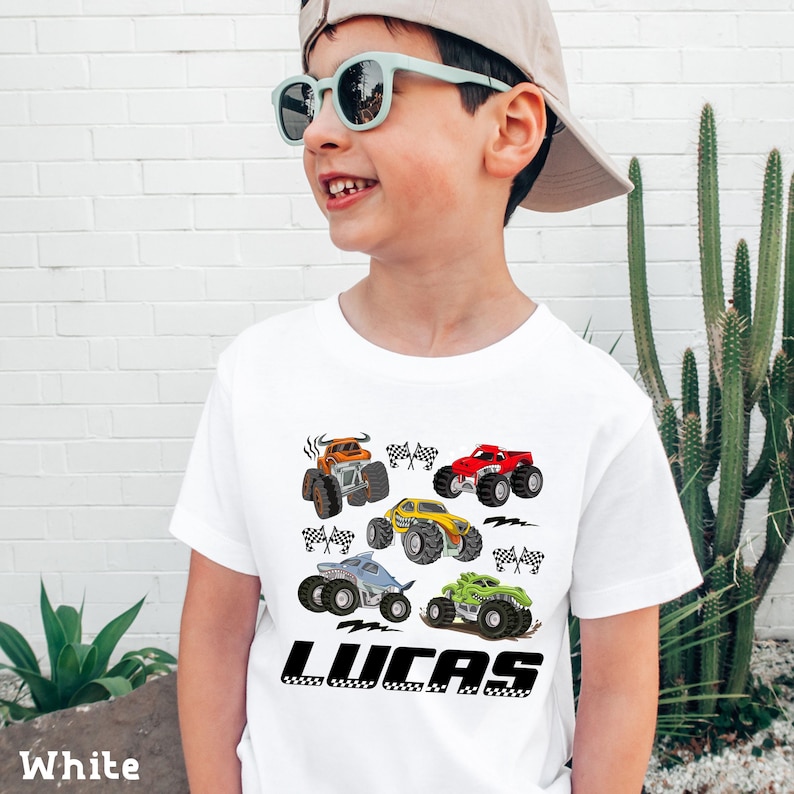 A young boy wearing a white t-shirt with a graphic of colorful monster trucks and the name "Lucas" printed on it.