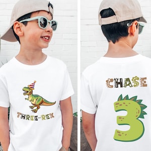 A young boy wearing a white t-shirt with a dinosaur graphic and the text "Three Rex" printed on it.