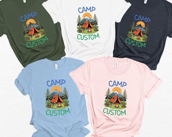 May include: Five short-sleeved t-shirts in various colors: olive green, white, navy blue, light blue, and pink. Each shirt features a camping-themed graphic with a tent, mountains, and the words "CAMP" and "CUSTOM" in a playful font.