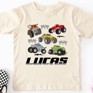 A white t-shirt with a graphic design of various monster trucks and checkered flags, along with the name "LUCAS" printed below.