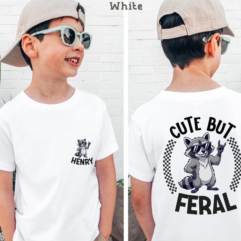 A young boy wearing a white t-shirt with a graphic of a raccoon and the text "CUTE BUT FERAL" printed on it.