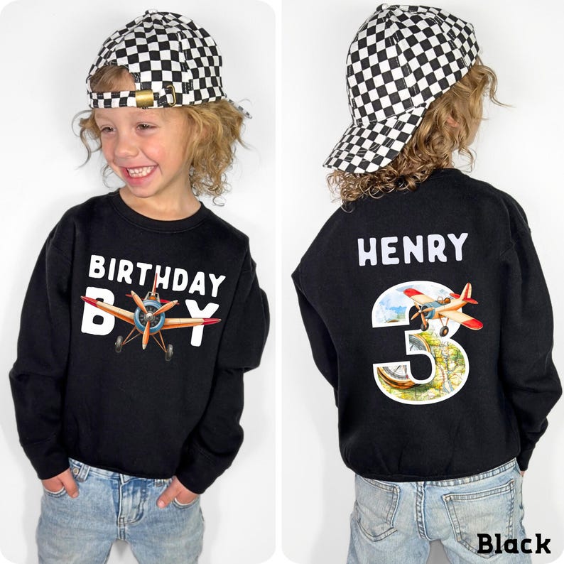 A young boy wearing a black sweatshirt with a checkered hat and a birthday shirt with a plane design, smiling at the camera.